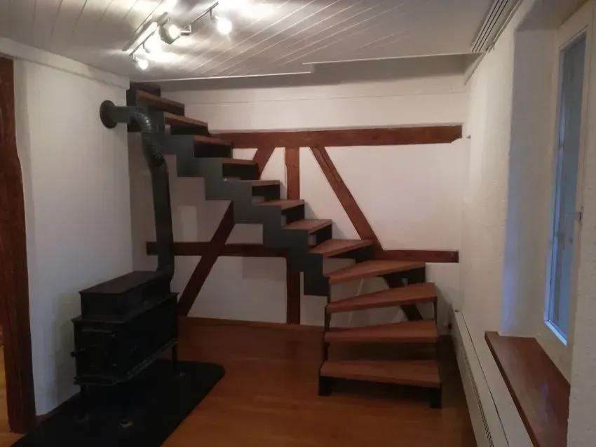 Kompakte Treppe mit dunklen Holzstufen und schwarzem Geländer in einem schmalen weißen Raum