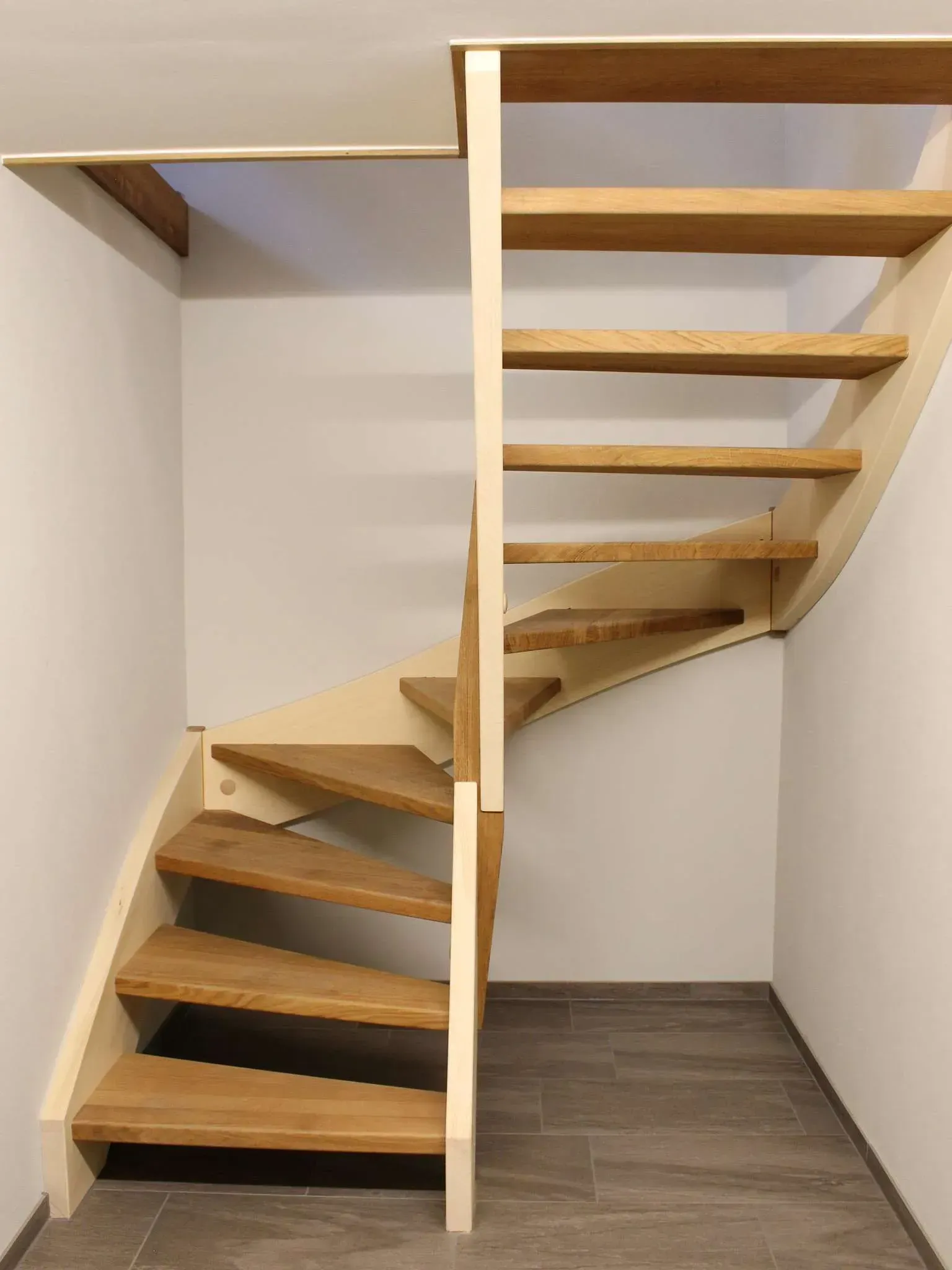 Schwebende hölzerne Wendeltreppe in einem kleinen weißen Raum mit grauem Boden