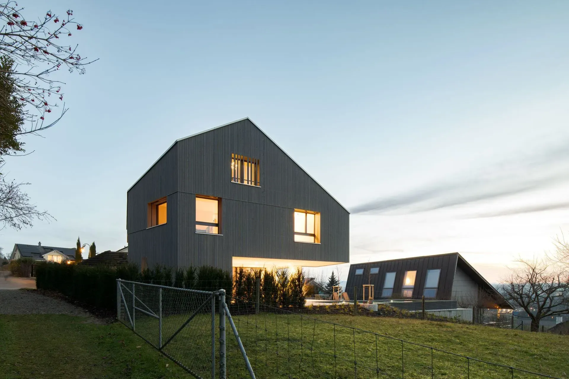 Modernes dunkelgraues Haus mit beleuchteten Fenstern auf einem grasbewachsenen Hügel in der Abenddämmerung
