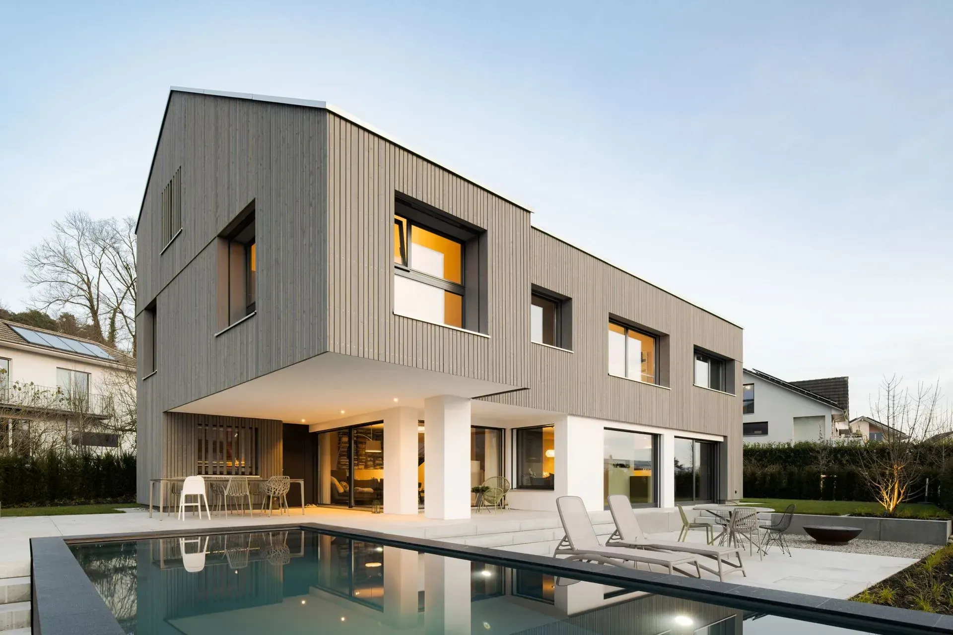 Modernes graues zweistöckiges Haus mit Pool und Terrasse in der Abenddämmerung