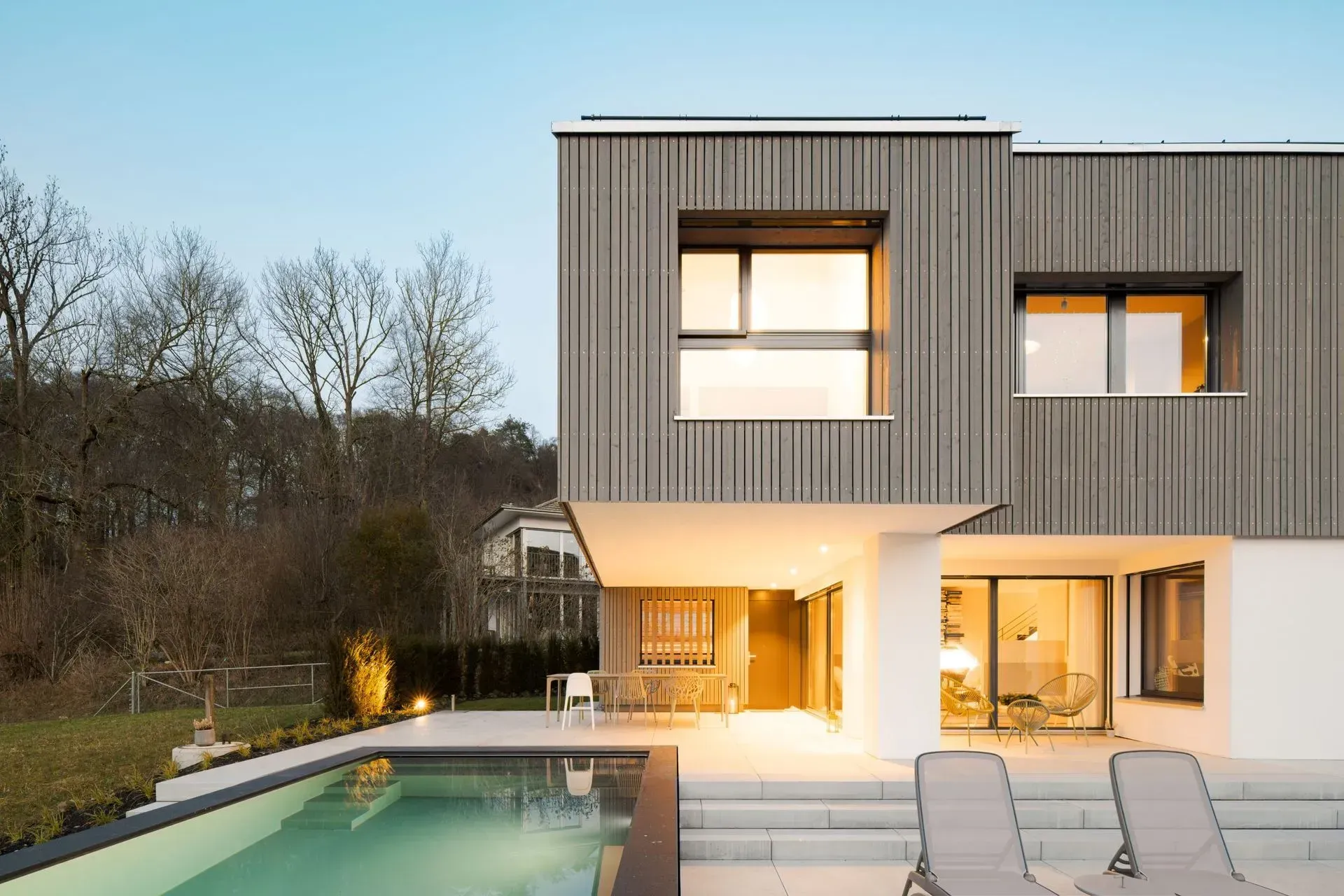 Modernes zweistöckiges Haus mit beleuchtetem Pool und Terrasse in der Abenddämmerung