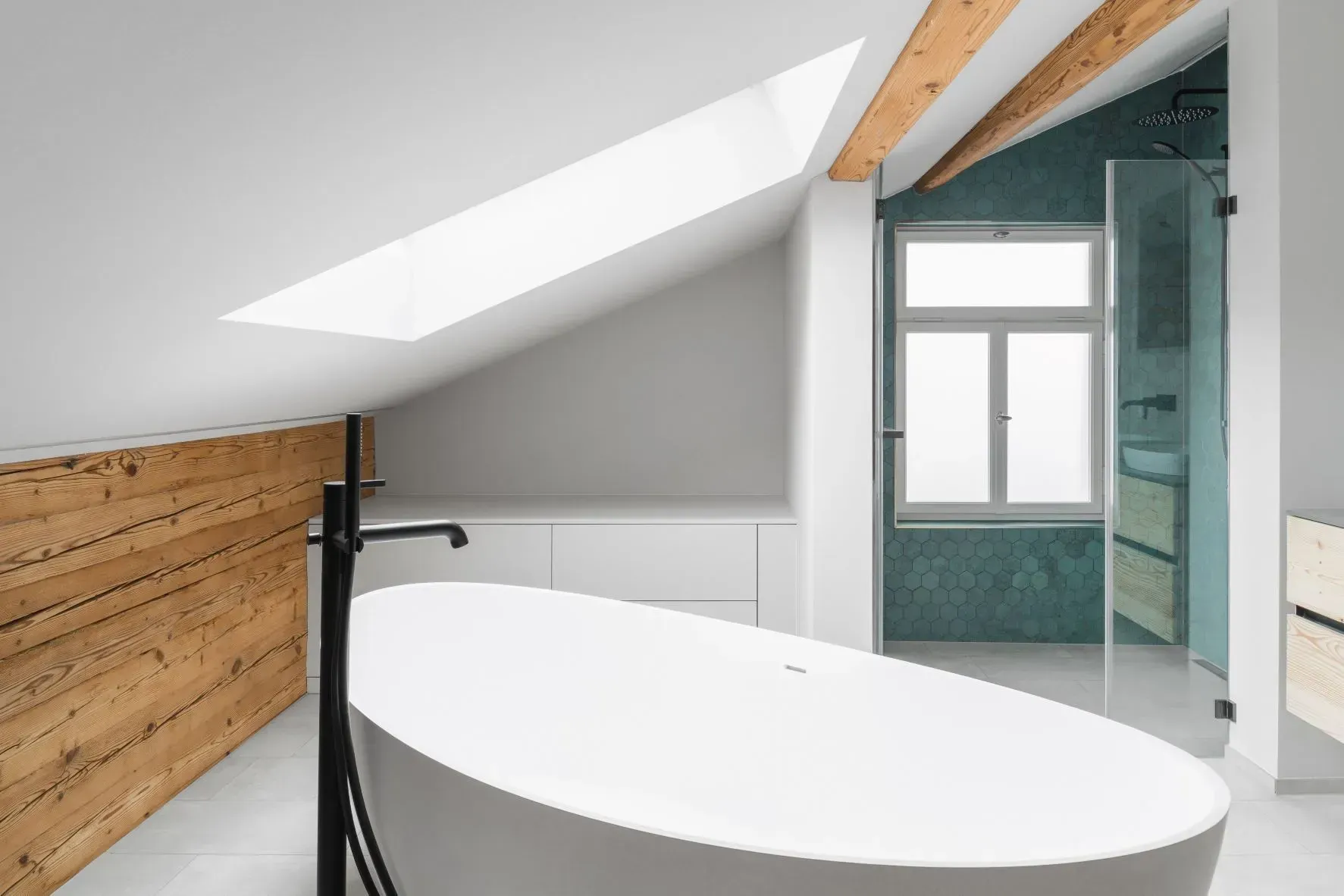 Modernes Dachgeschossbadezimmer mit Dachschräge, weißer Badewanne, Holzelementen und Glasdusche.