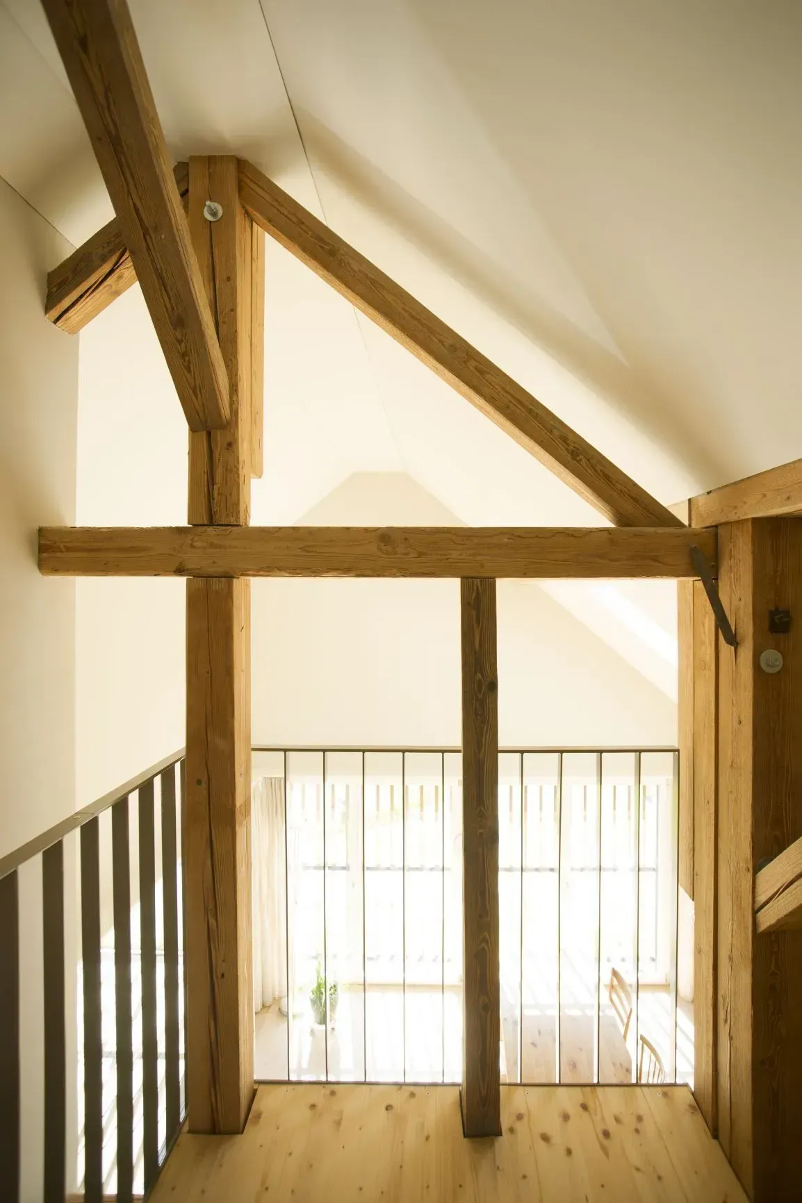 Loft-Interieur aus Holz mit freiliegenden Balken und einem hellen Fenster mit Blick auf ein darunterliegendes Geländer.
