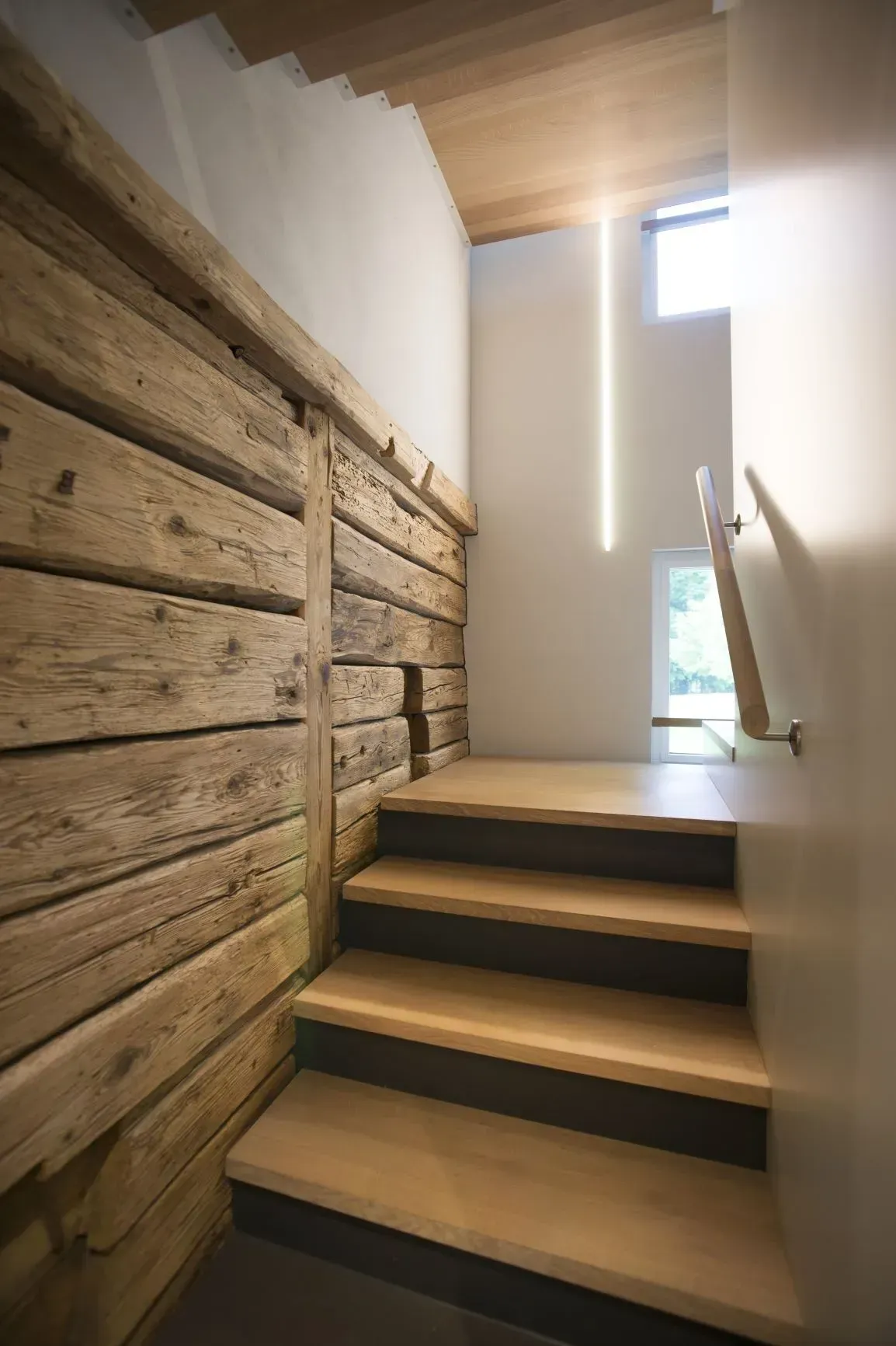 Modernes Treppenhaus mit Holzwand, leichten Stufen und hohem Fenster neben einem Handlauf