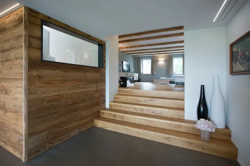 Modernes Interieur mit holzgetäfelter Wand, offener Treppe und Blick in ein helles Wohnzimmer