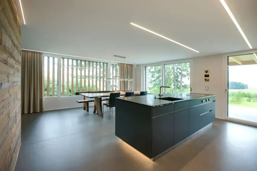 Moderne offene Küche mit Essbereich, dunkler Kochinsel, großen Fenstern und Glasschiebetüren zur Terrasse.