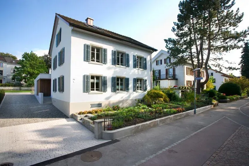 Weißes Haus mit grünen Fensterläden und einem gepflegten Vorgarten in einer ruhigen Wohnstraße