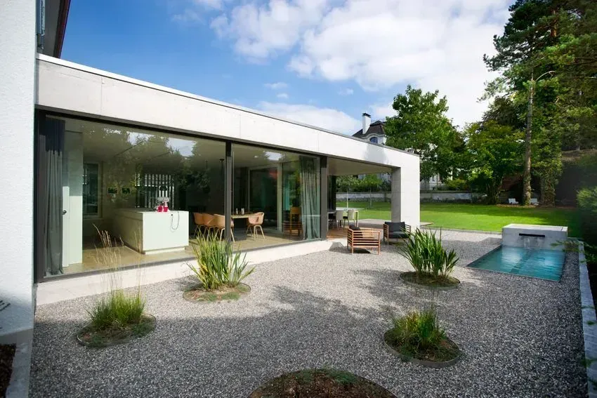 Moderne Hausterrasse mit Kiesgarten, Glastüren und kleinem blauen Pool