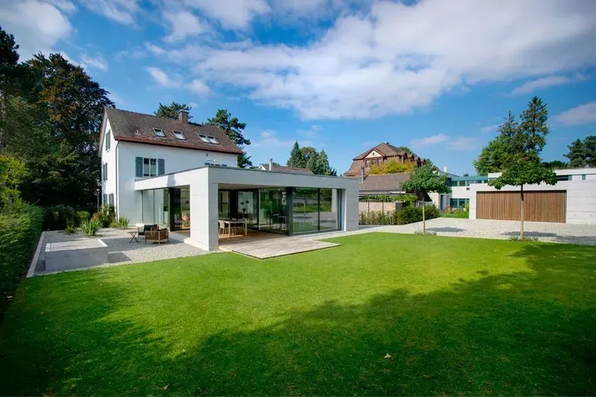 Modernes Haus mit großem grünen Rasen, Terrasse und teilweise bewölktem blauen Himmel