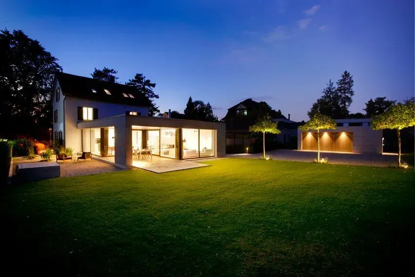 Modernes Haus mit beleuchteter Terrasse und großem grünen Rasen in der Abenddämmerung