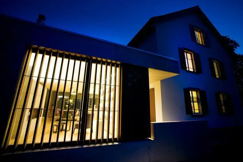 Modernes Hausäußeres bei Nacht mit warmer Innenbeleuchtung und einer hohen, schwarzen Lamellenfassade