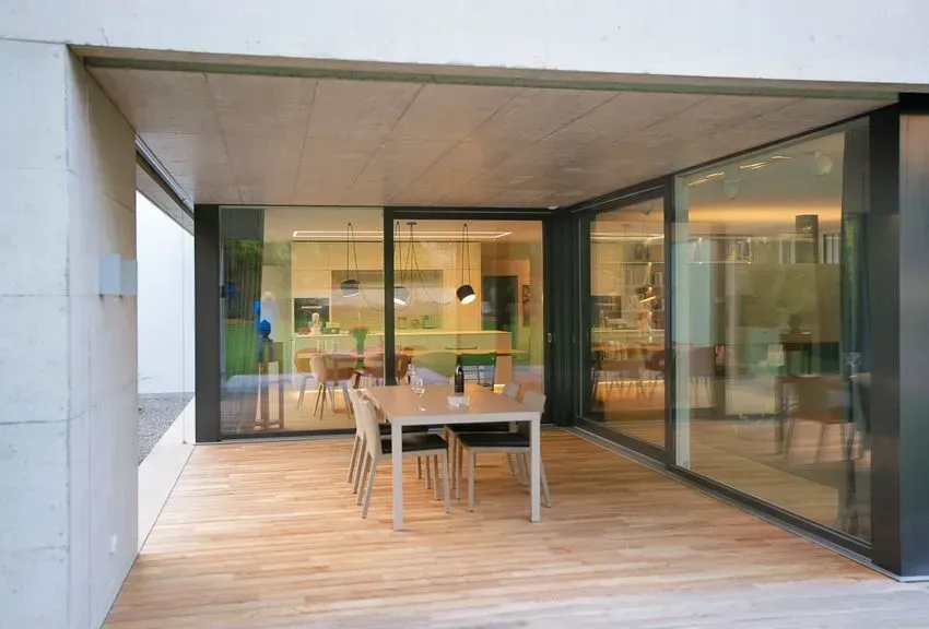 Moderne Terrasse mit Holzdeck, Esstisch und Glasschiebetüren mit Blick auf einen Innenraum