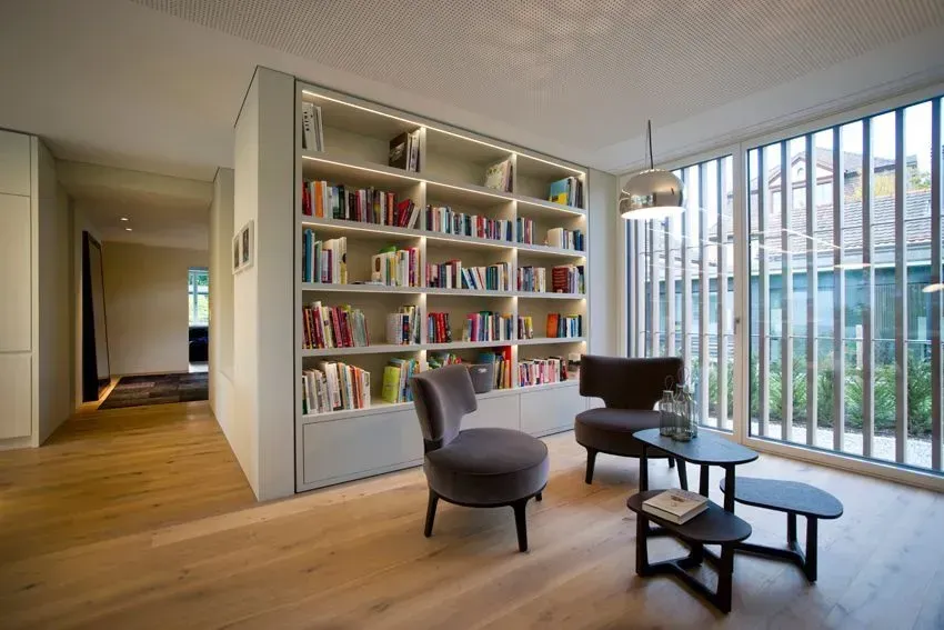 Modernes Wohnzimmer mit eingebauten Bücherregalen, Loungesesseln und großen Fenstern mit Blick ins Grüne