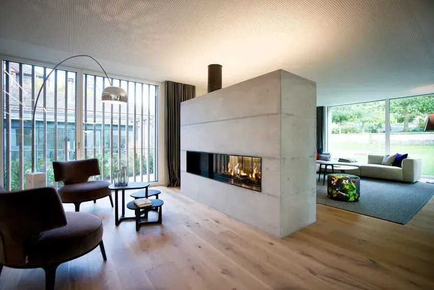 Modernes Wohnzimmer mit zentralem Kamin, Holzböden und großen Fenstern mit Blick ins Grüne