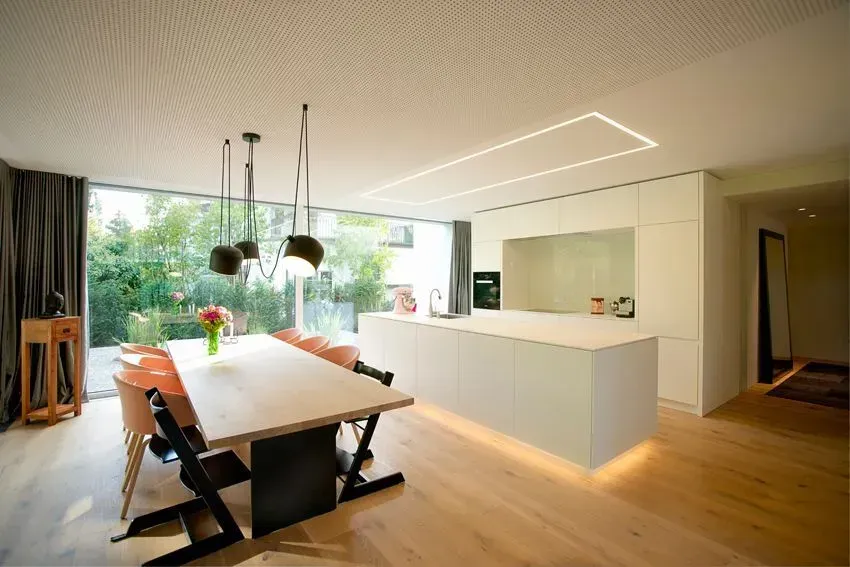Modernes Esszimmer mit Holztisch, schwarzen Stühlen, Pendelleuchten und offener Küche in hellem Tageslicht