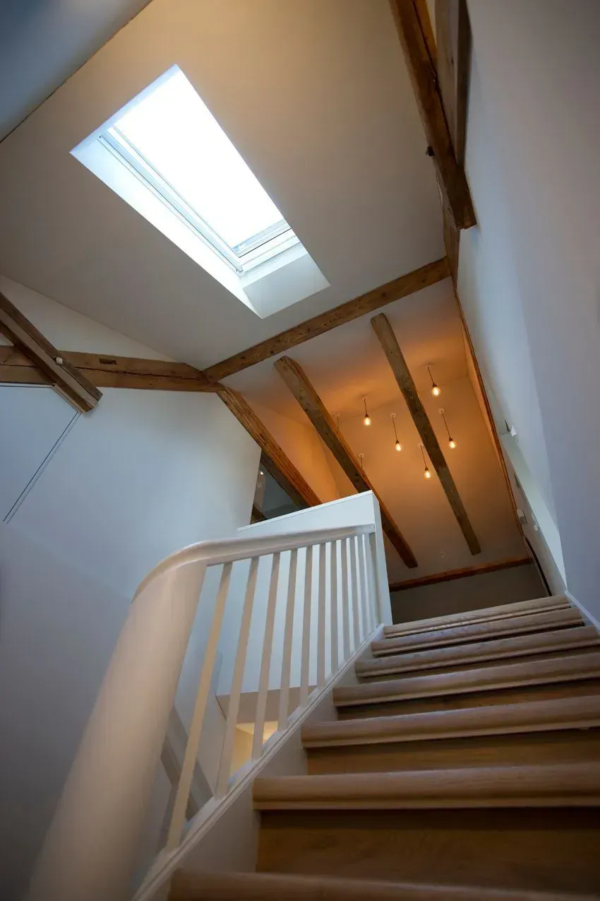 Treppe mit weißem Geländer unter einem Oberlicht in einem schmalen Flur mit freiliegenden Holzbalken