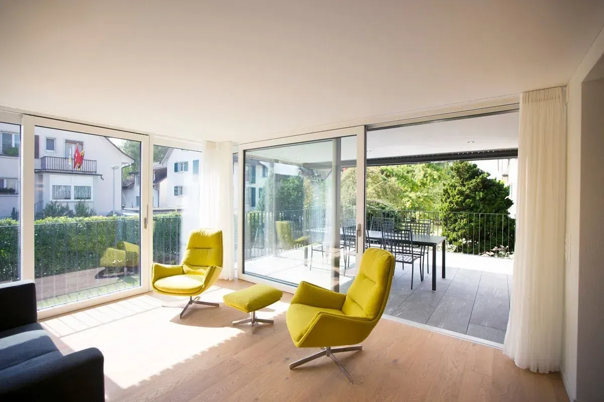Modernes Wohnzimmer mit gelben Sesseln, großen Fenstern und Blick auf Terrasse und Garten