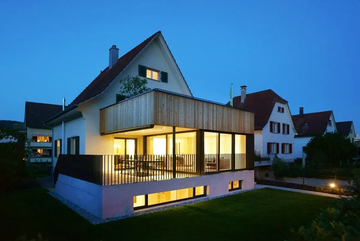 Modernes Haus, das in der Abenddämmerung mit warmem Innenlicht und einem blauen Abendhimmel erstrahlt