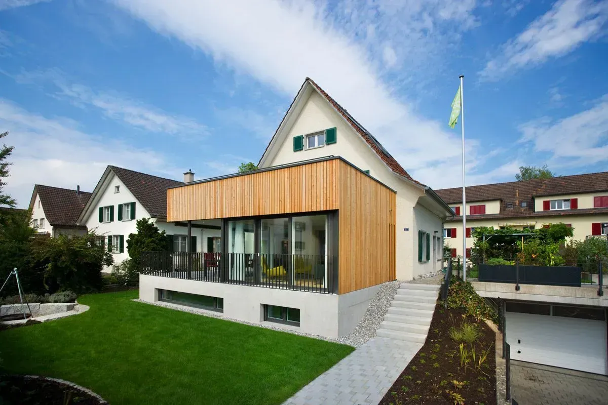 Modernes Haus mit Holzverkleidung, großen Fenstern und einem grünen Rasen unter blauem Himmel