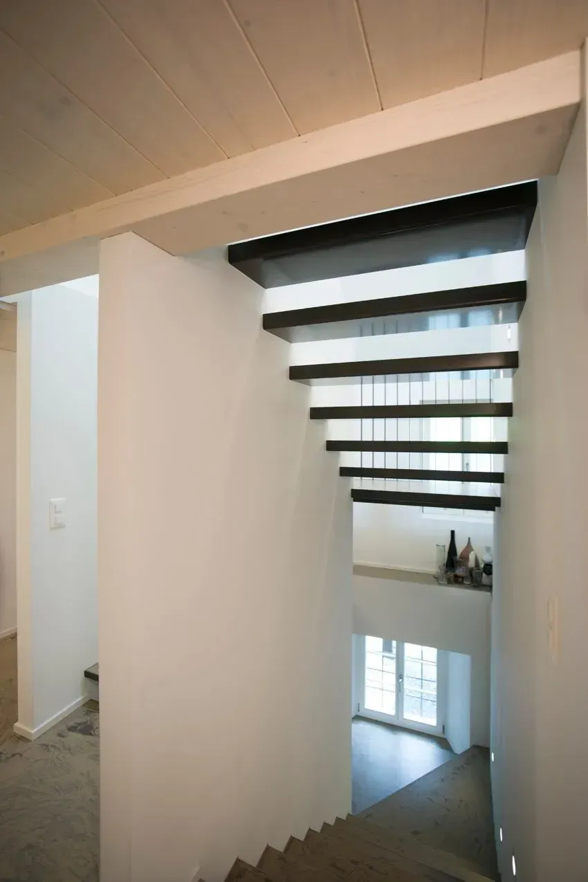 Treppenhaus mit weißen Wänden, schwarzen Stufen und großen Oberlichtern, die Tageslicht hereinlassen