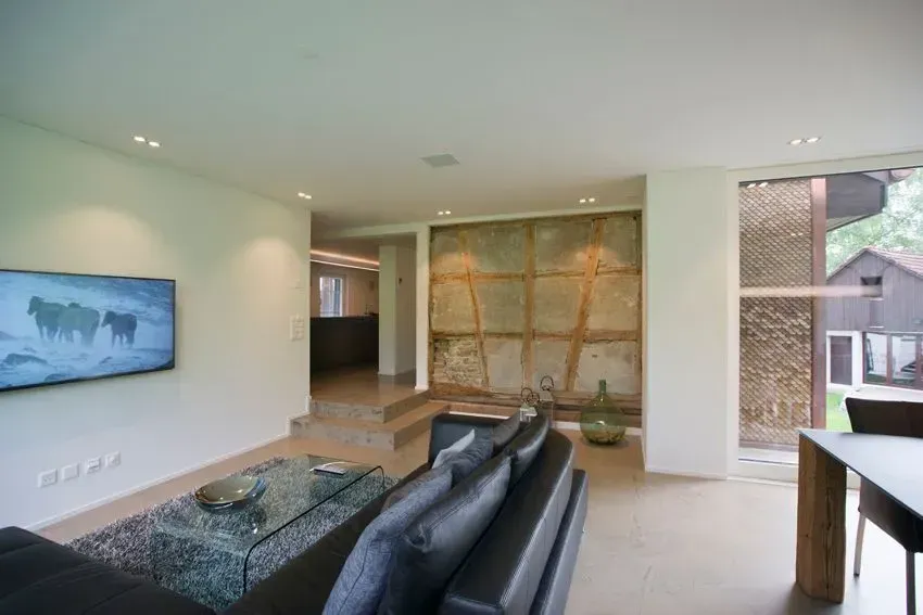 Modernes Wohnzimmer mit schwarzem Sofa, Glas-Couchtisch, an der Wand montiertem Fernseher und Schiebetüren zur Terrasse