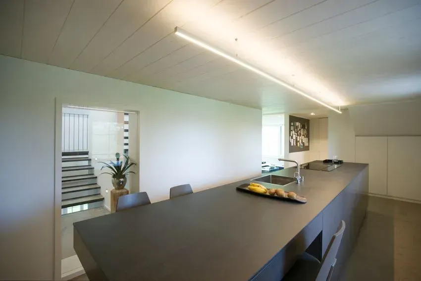 Moderne Küche und Essbereich mit einem langen dunklen Tisch, Treppe und großen Fenstern mit Jalousien.