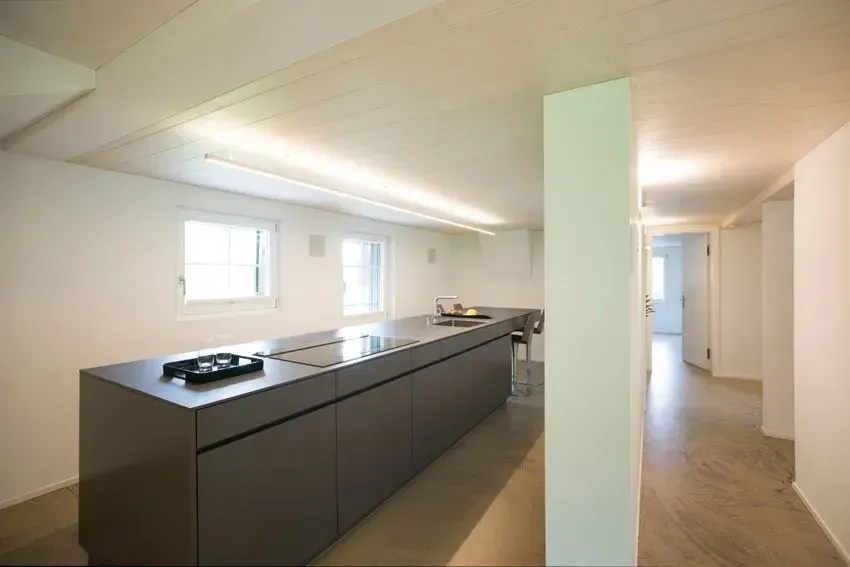 Moderne offene Küche mit dunkler Kochinsel, weißen Wänden und Flur, der zu den Zimmern führt