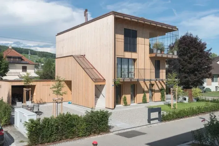Modernes zweistöckiges Holzhaus mit großen Fenstern, Balkon und kleinem Garten in einer ruhigen Straße