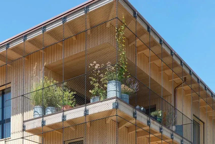 Moderne Wohnhausfassade mit Balkonen, Topfpflanzen und Holzlamellenverkleidung vor blauem Himmel