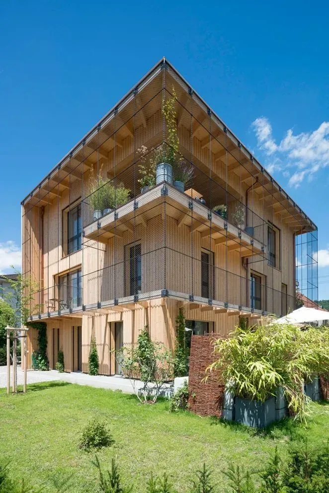 Modernes, mehrstöckiges Holzhaus mit schrägem Dach und grünem Rasen unter blauem Himmel