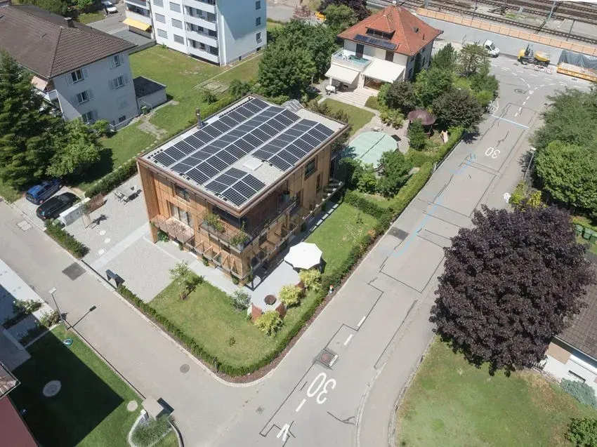 Luftaufnahme eines modernen Hauses mit Solarpaneelen, einem grünen Garten und den umliegenden Wohnstraßen.
