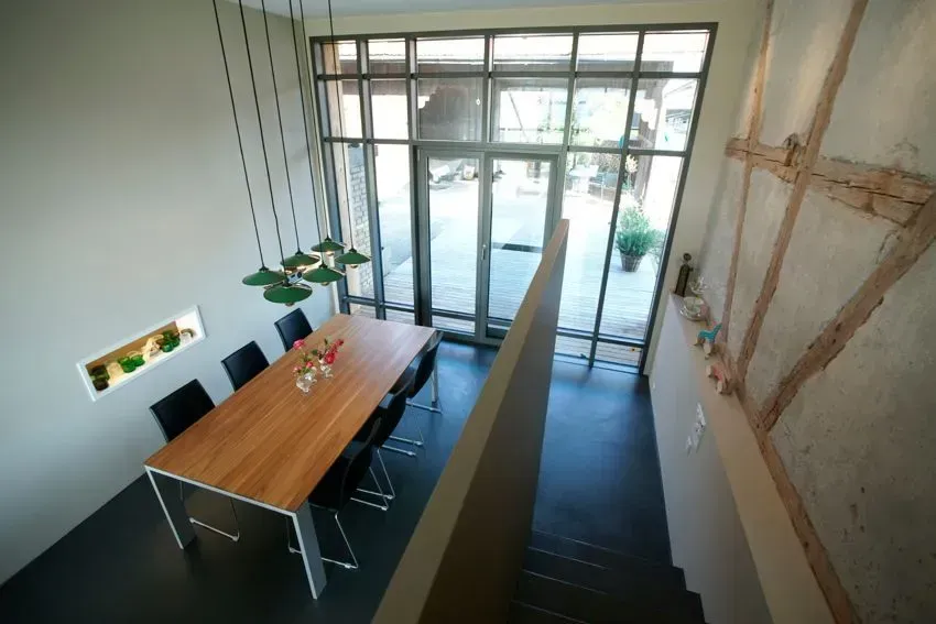 Modernes Esszimmer mit langem Holztisch, schwarzen Stühlen und großen Glastüren mit Blick auf eine Terrasse