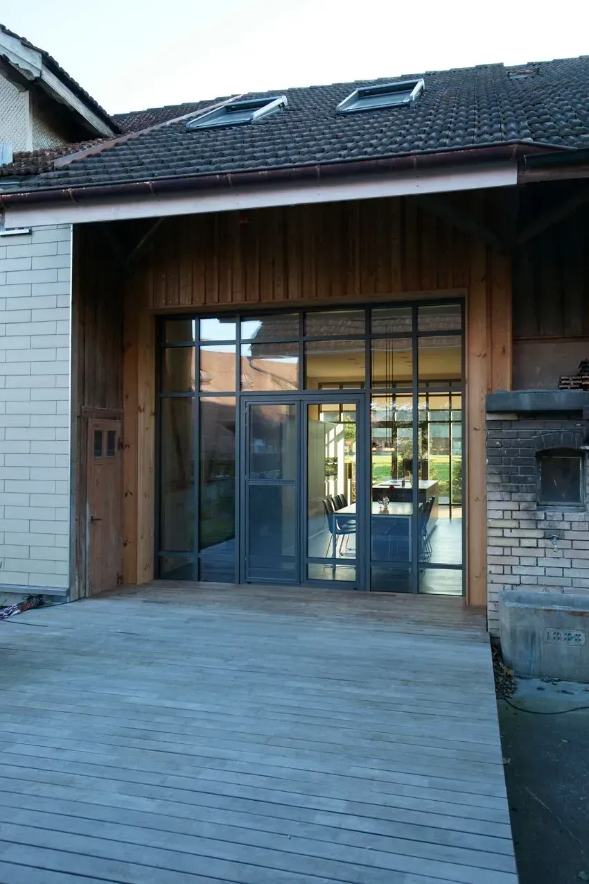 Moderner Hauseingang mit Glastüren, Holzverkleidung und einem im Bau befindlichen Ziegeldach