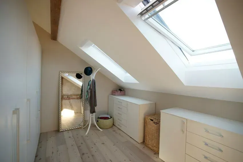 Helles Dachzimmer mit Dachfenster, Dachschräge, weißen Schränken, Spiegel und Kleiderstange