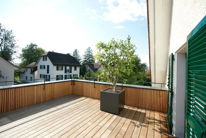 Holzterrasse auf dem Dach mit Topfbaum, Geländer und Nachbarhäusern im Hintergrund