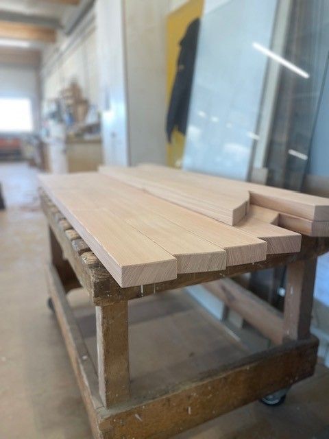 Ein Stapel leichter Holzbretter auf einer fahrbaren Werkbank in einer Werkstatt.