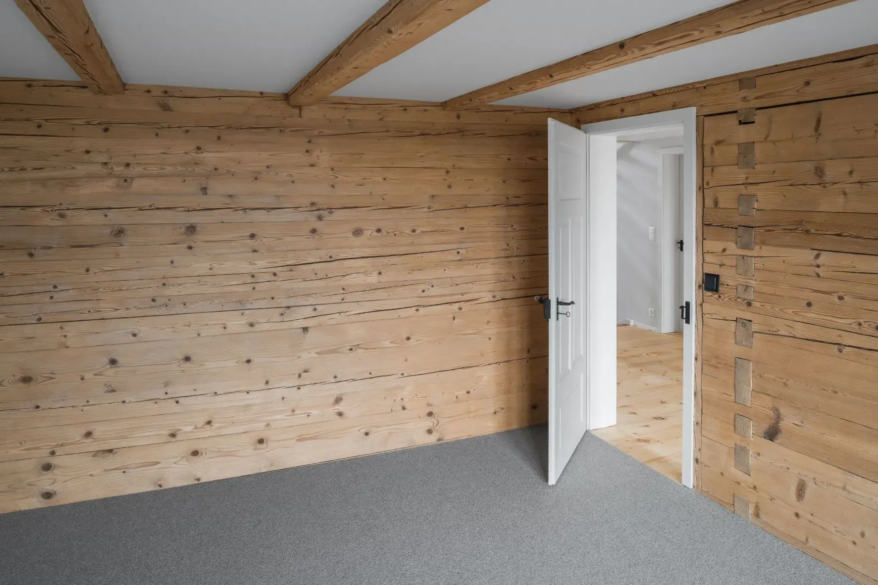 Leeres, holzgetäfeltes Zimmer mit grauem Teppichboden und offener weißer Tür.