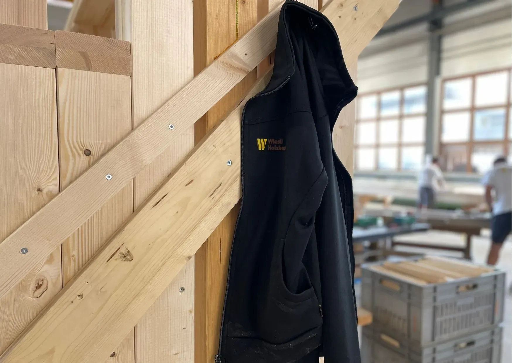 Eine schwarze Jacke hängt in einer Werkstatt an einem hölzernen Treppengeländer.