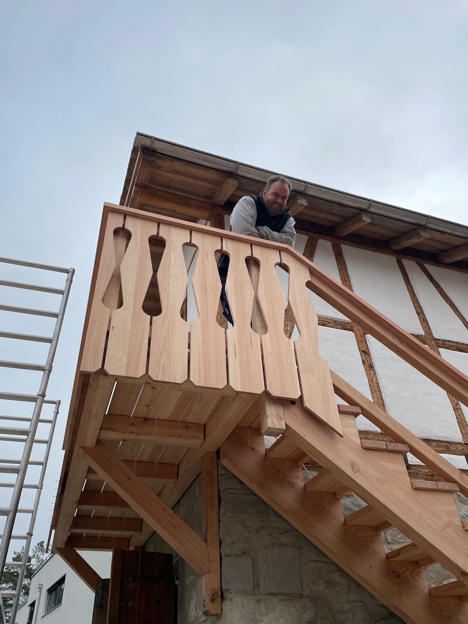 Eine Person lehnt sich über einen hölzernen Balkon an einer Außentreppe
