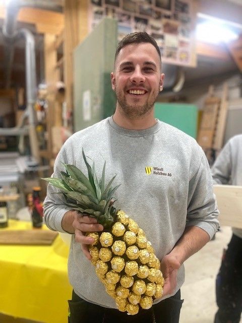 Ein lächelnder Mann hält in einer Werkstatt eine Ananas-Beeren-Sorte, eine ananasförmige Anordnung gelber Beeren.