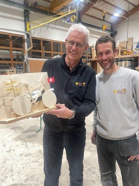 Zwei Männer in einer Werkstatt halten ein großes beigefarbenes 3D-gedrucktes Modell und lächeln in die Kamera.