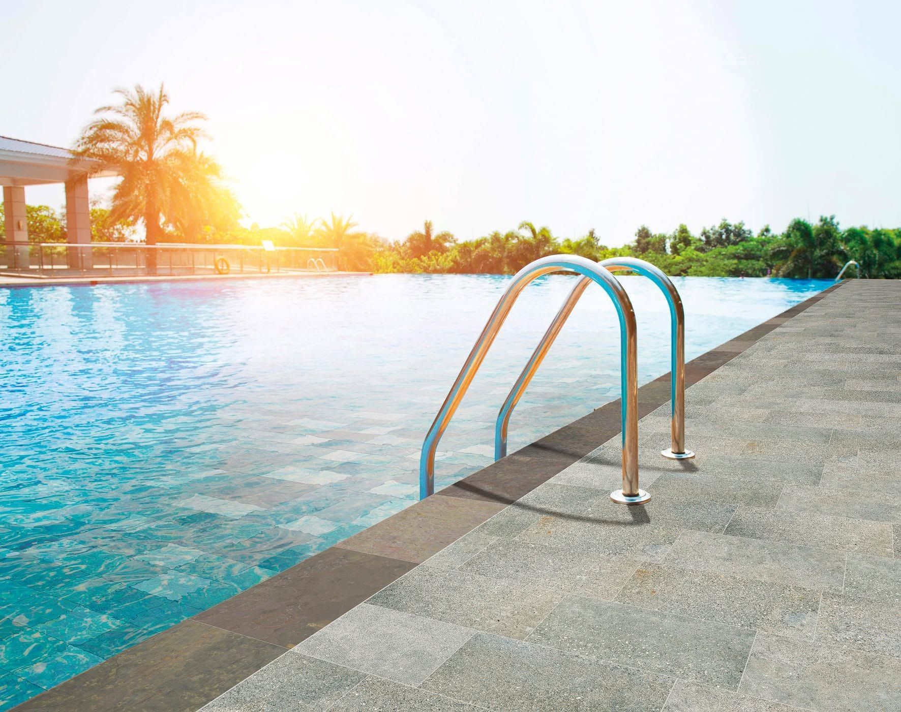 Piscine extérieure avec échelle métallique et vue ensoleillée sur un complexe hôtelier tropical.