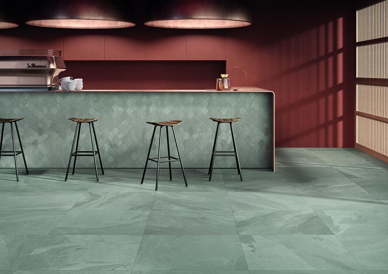 Bar moderne vide avec comptoir en pierre grise, trois tabourets et murs rouges éclairés par des suspensions lumineuses.