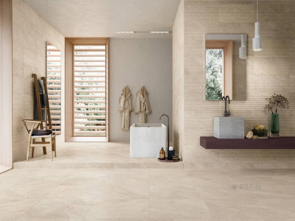 Salle de bains beige avec douche à l'italienne, tabouret en bois, miroir et serviettes suspendues.
