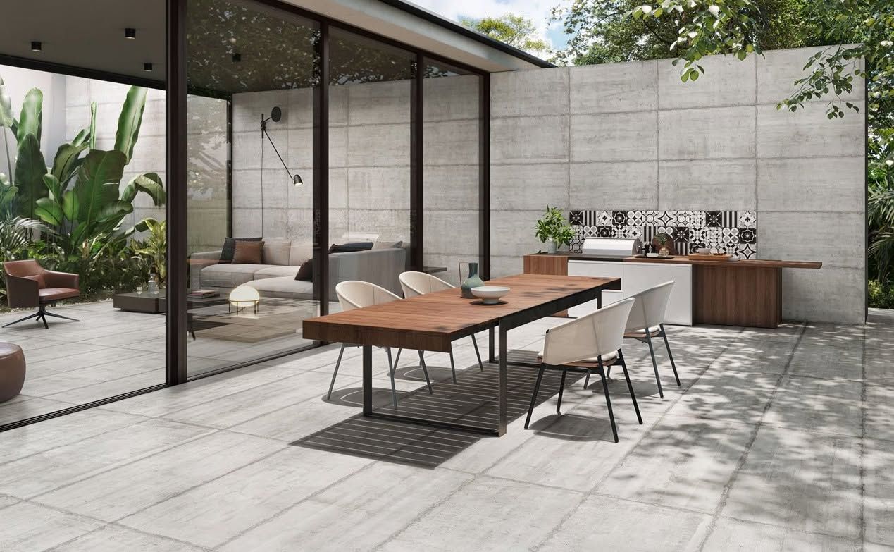 Terrasse extérieure avec parois vitrées, table à manger, chaises longues et barbecue intégré adossé à des murs en pierre.