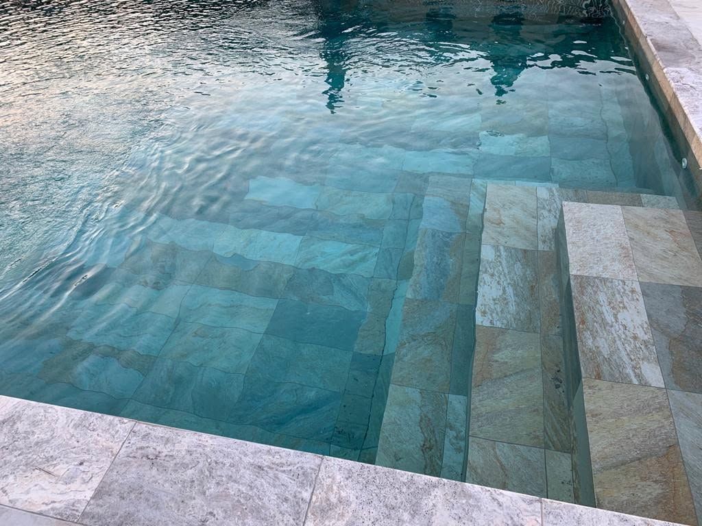 Piscine carrelée de bleu, à l'eau claire et aux bords en pierre blanche