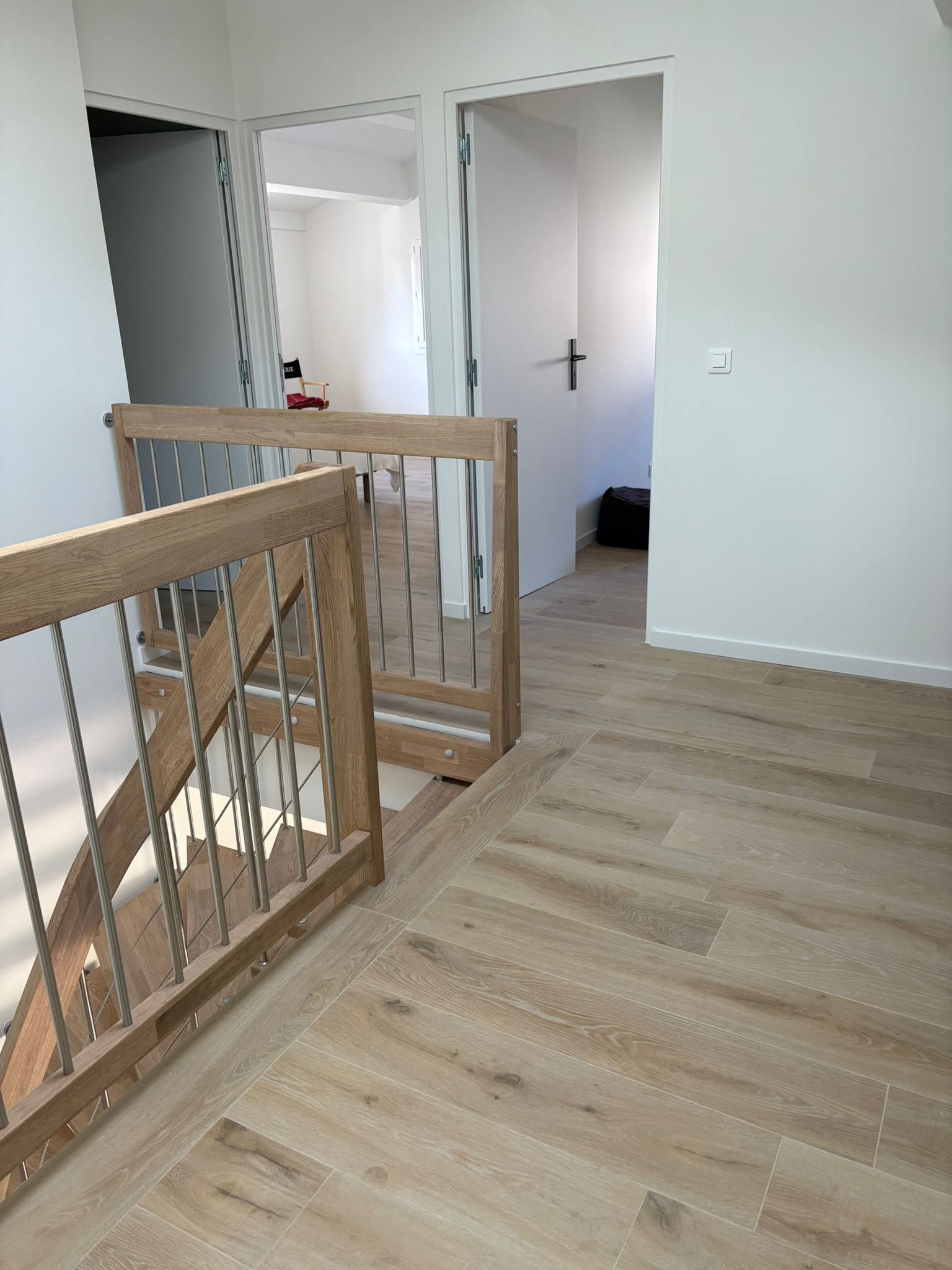 Couloir intérieur avec parquet clair, rampe d'escalier en bois et portes ouvertes donnant sur des pièces adjacentes