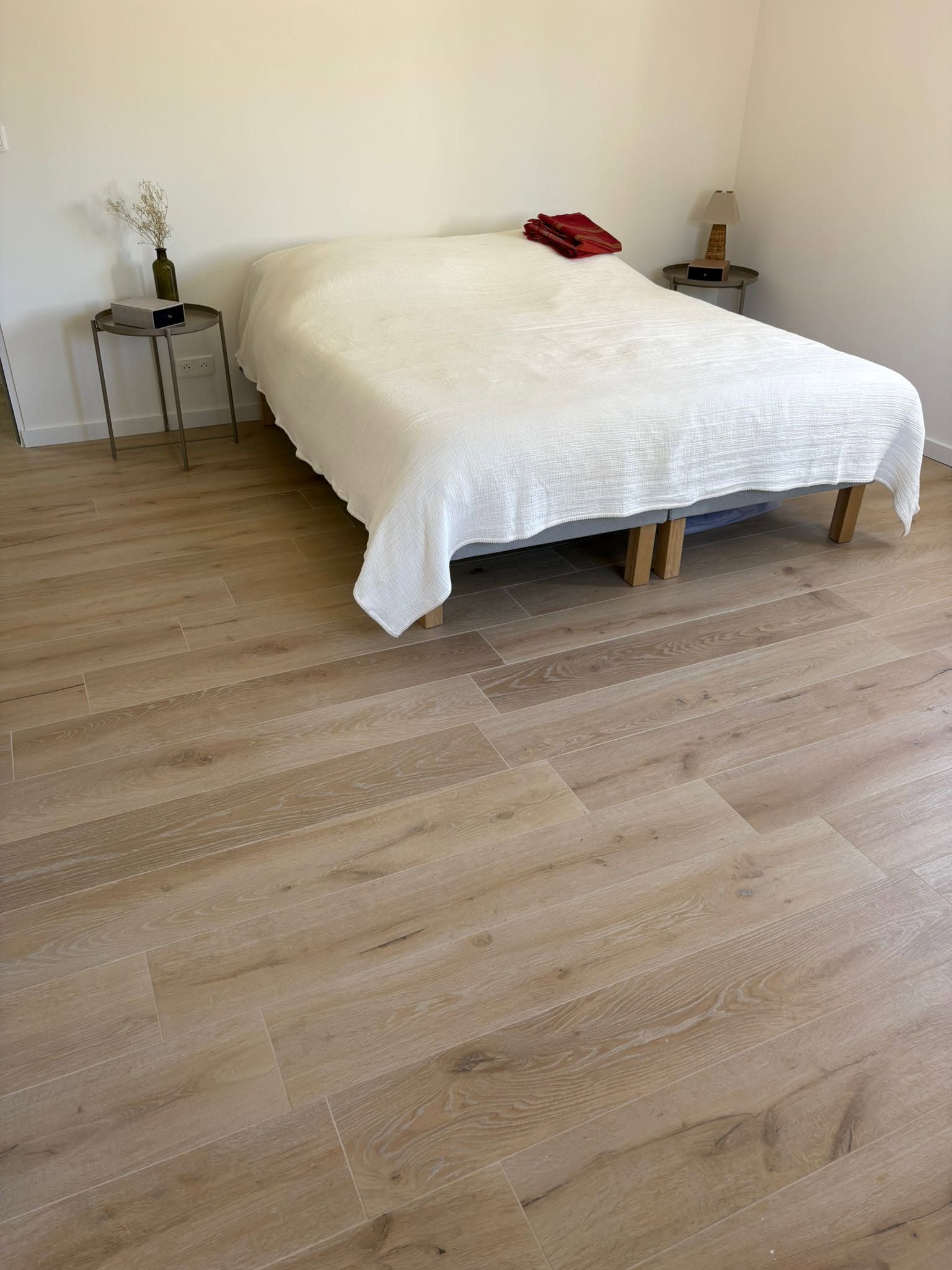 Chambre minimaliste avec un couvre-lit blanc, un parquet clair et de petites tables de chevet de chaque côté.