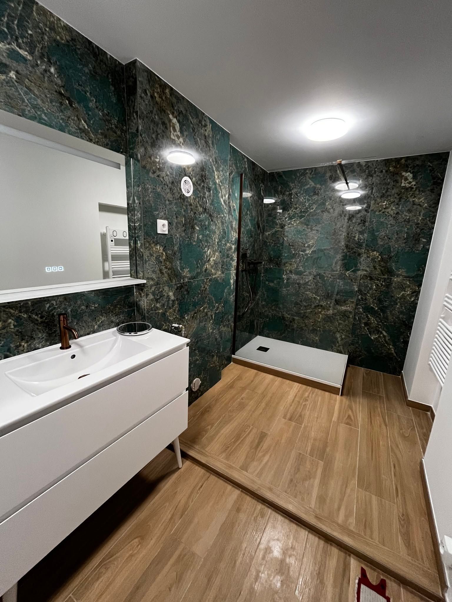 Salle de bains moderne avec murs en marbre foncé, meuble-lavabo blanc, parquet, miroir et douche à l'italienne.