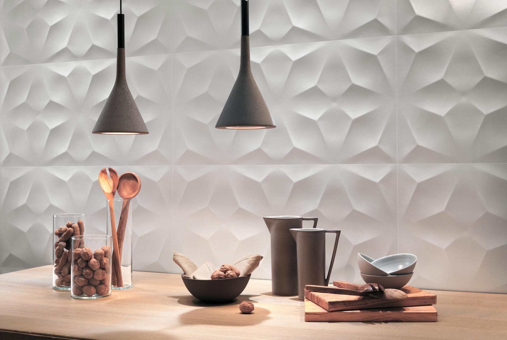 Plan de travail de cuisine moderne avec ustensiles, bols, bocaux et suspensions lumineuses sur un mur blanc texturé